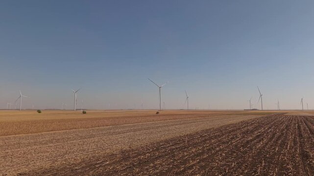 Low Drone Flight Over Plowed Furrows Toward Distant Wind Turbines