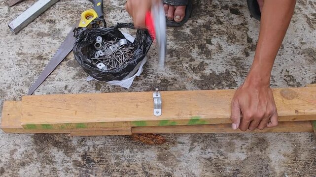 Man using red claw hammer to attach metal bracket onto wooden board