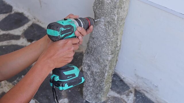 Close-up view of drilling into rough stone surface using hand held cordless power drill