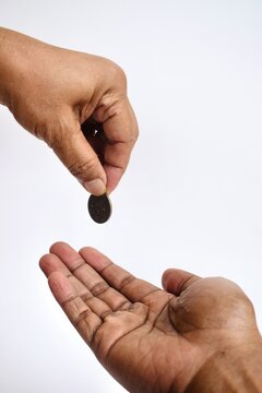 High-angle view of a hand dropping a single coin into another open palm below against a neutral white background, representing charity, payment, or financial assistance.