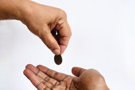 High-angle view of a hand dropping a single coin into another open palm below against a neutral white background, representing charity, payment, or financial assistance.