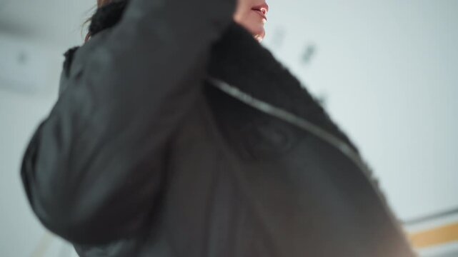 Medium shot focuses on back of woman with wavy brown hair wearing black jacket capturing her movements and details like zipper texture. background is softly lit