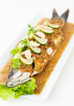 Thai steamed whole sea bass, spicy lime sauce, garlic, chili, and coriander topping on a traditional ceramic plate, authentic exotic seafood dish, steamed seabass with lemon sauce