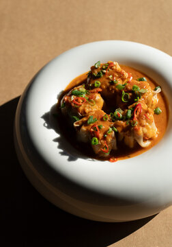 Delicious dumplings served in a bowl with a spicy sauce and green onions, savor rich, steaming dumplings soup, culinary dumplings delight, Dumplings coated in a spicy red-orange sauce