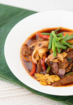 Asian-style meat and mushroom stir-fry with red pepper and spring onions in a rich savory sauce, served in a white bowl on a banana leaf in bright light, ideal for restaurant menus and food promotion.