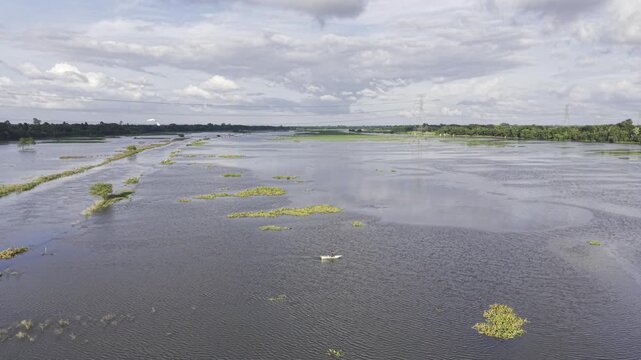 Aerial view of a person traveling by a small traditional boat through flooded agricultural fields at Nandiar Bil in Kushtia, Bangladesh, during the monsoon season.
