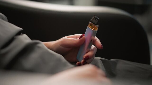 Close up view shows hands with red nail polish holding electronic vaping device focusing on grip and details like liquid level vape handheld smoking nicotine