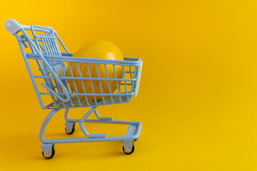Single lemon in miniature shopping cart on yellow background © Irina