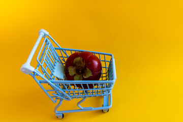 Single ripe persimmon in miniature shopping cart on yellow background © Irina