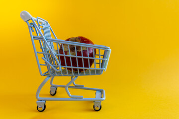 Wide angle of lone persimmon in miniature shopping cart against yellow backdrop © Irina