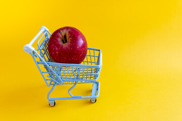 Crisp red apple centered in miniature cart on solid yellow background © Irina