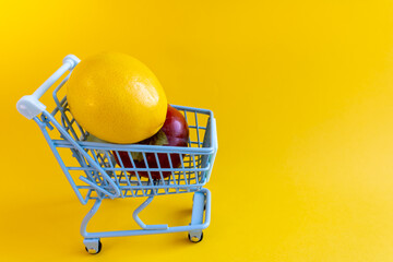 Yellow lemon towers over dark red fruit in tiny cart on yellow backdrop © Irina