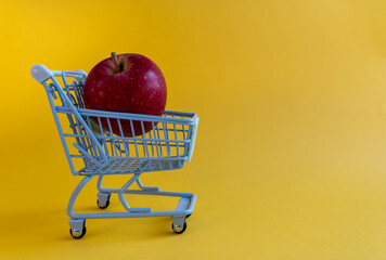 Single red apple inside miniature shopping cart on yellow background © Irina