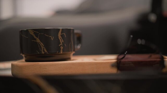 Close up view shows black marble patterned mug on wooden tray accompanied by sunglasses. composition emphasizes still life arrangement in indoor domestic environment