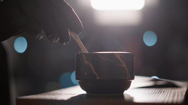 Gloved hand pours hot beverage into marble patterned cup with soft lighting and bokeh background. focus is on precise pouring motion and texture details of both hands and objects
