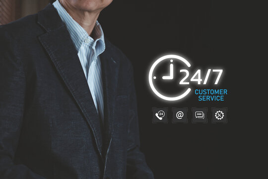 Businessman standing next to 24/7 customer service glowing hologram overlay. Concept of continuous online support, client helpdesk, call center contact, and technical assistance