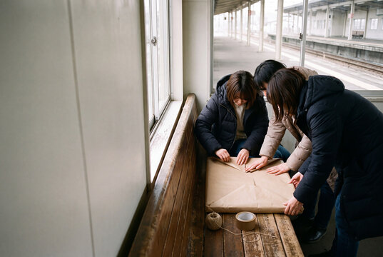 Women Wrapping Brown Paper Parcel on Station Bench