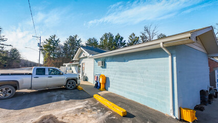Small town convenience store with a silver pickup truck parked outside. The building features a light blue painted cinder block wall. Sunny rural roadside setting for local business © SMHT ART WORKS