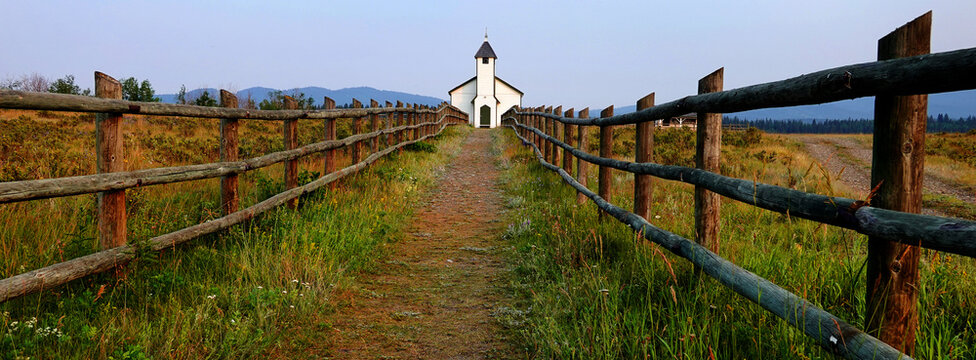 Old Christian Church with Cemetery and Headstones in Rural Location with Grassy Field and Blue Mountains in Background