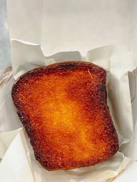 Close up of a golden brown caramelized thick slice of butter toast on white parchment paper inside a takeout box