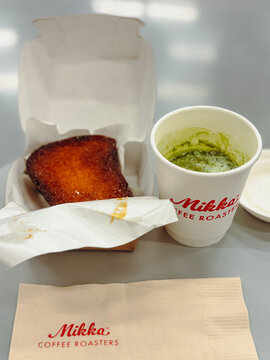 Bangkok, Thailand - October 7, 2026: Takeout set from Mikka Coffee Roasters featuring a cup of hot matcha green tea and a thick slice of caramelized honey toast in a paper box.