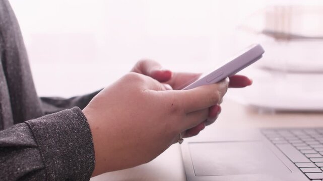 Mobile typing. Information technology. Unrecognizable female manager using smartphone for business planning at office desk with laptop at workplace.