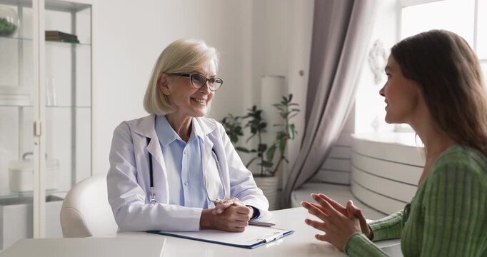 Experienced woman physician discussing health concerns with female patient providing supportive guidance encouraging dialogue addressing concerns showing professional care during clinic appointment
