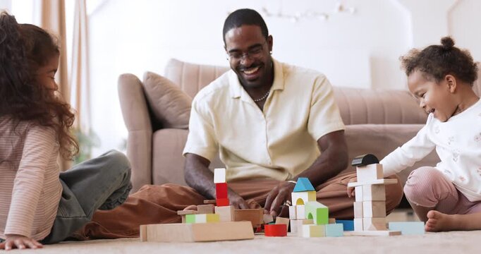 Involved African father playing with cubes with two little daughters on floor helping children build towers using educational toys encouraging playful home learning enjoying creative family activity