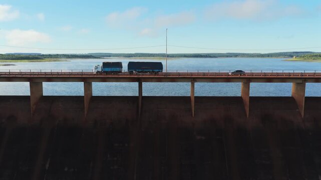 Linear geometry of the concrete bridge structure spans the dark water reservoir as a transport truck drives across.