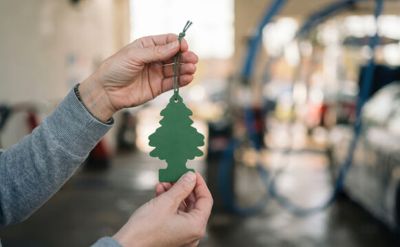 Person holding a green tree air freshener in a car wash, representing vehicle maintenance and pleasant scent