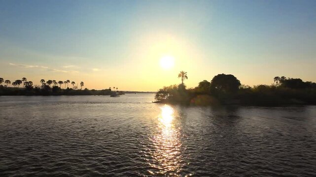 Sunset cruise on the Zambezi River near Victoria Falls, Zimbabwe, with golden reflections, silhouetted palms and a boat in the distance.