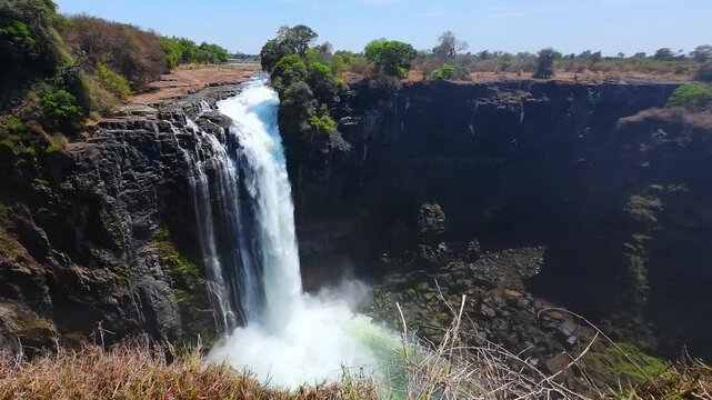 Water plunges over exposed cliffs into a mist-filled gorge at Victoria Falls, Zimbabwe, during the dry season.