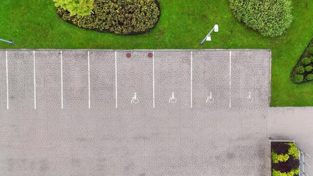 Top-down drone view of empty wheelchair-designated parking spaces beside manicured lawns, shrubs and patterned paving in a clean organized setting.