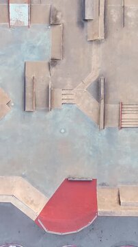 Straight-down drone view of an empty skatepark street section with stairs, banks, ledges, rails and a red platform arranged in a technical urban obstacle course.