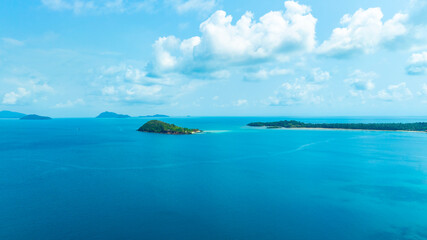 Fototapeta premium Panoramic aerial view of a lush green tropical island in the middle of a vast blue ocean under a bright sky with clouds, representing vacation, travel, and scenic nature.concept travel 