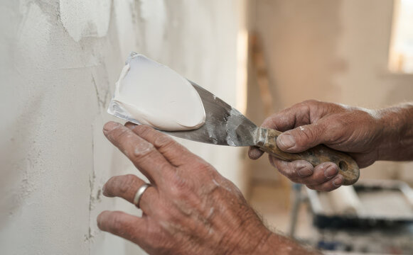 Middle-aged man plastering a wall with a putty knife for home renovation and interior design