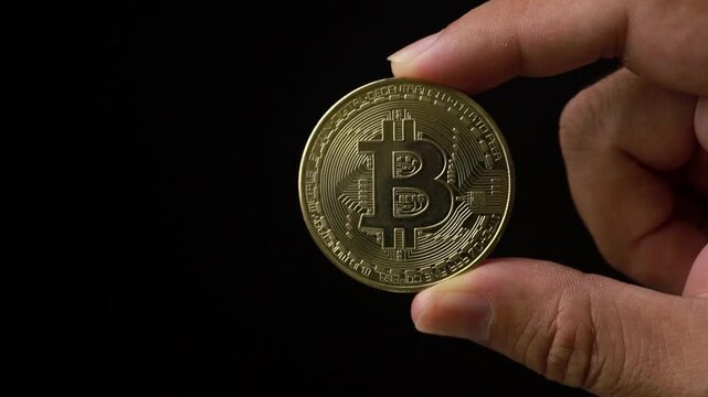Hand holding a gold bitcoin on a black background