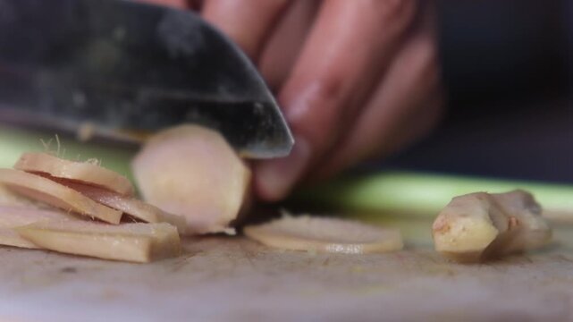 Close up footage of woman cutting fresh ginger root on wooden cutting board. One of ingredients for Tom Yam, Asian spicy soup. Cooking traditional food in kitchen at home.