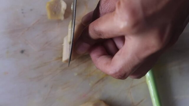 Close up footage of woman cutting fresh ginger root on wooden cutting board. One of ingredients for Tom Yam, Asian spicy soup. Cooking traditional food in kitchen at home.