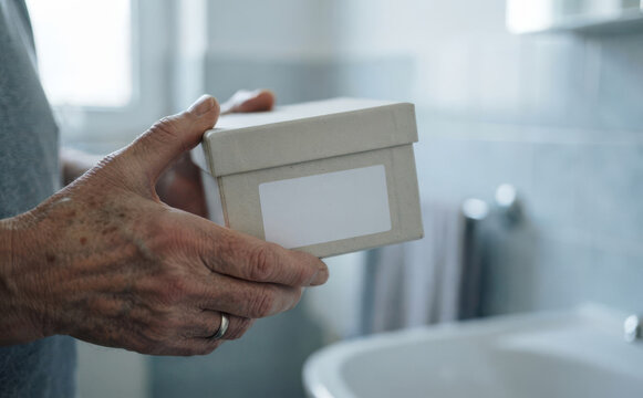 Senior man holding a small white cardboard box with a blank label in a bathroom