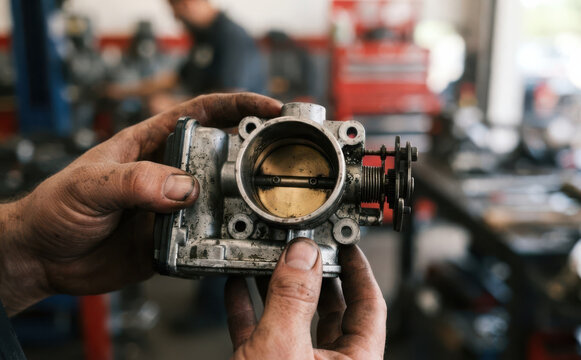 Mechanic holding a dirty car throttle body in an auto repair shop representing automotive maintenance and repair