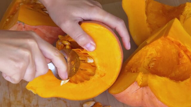 Hands cleaning pumpkin seeds with spoon on wooden board, top view close up. Autumn cooking process, fresh ingredients. Thanksgiving, Halloween.