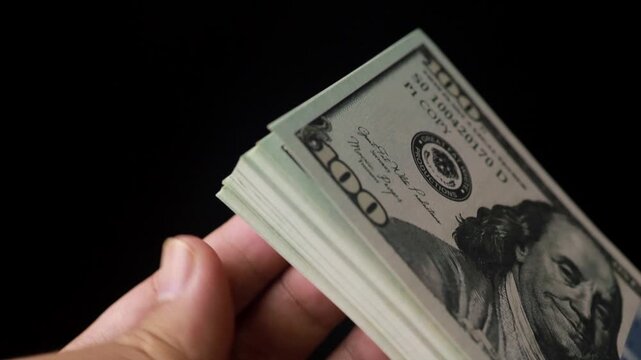 Hand flipping a thick stack of hundred dollar bills