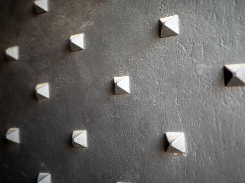 Macro close-up of black metal surface with decorative square pyramid studs, ideal for forged iron, industrial texture, historic hardware, geometric pattern and architectural design concepts.