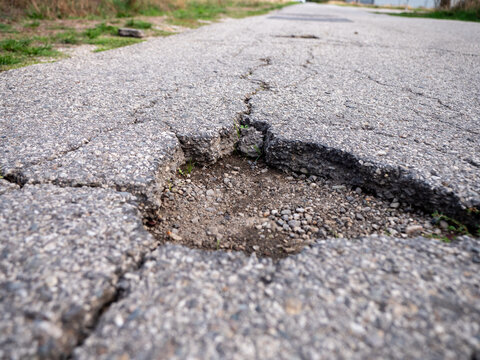 Large pothole in cracked asphalt exposing gravel and damaged road layers, ideal for road safety, infrastructure failure, maintenance, repair, transportation and public works concepts.