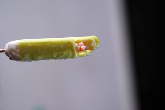 close-up macro view of a partially eaten ice cream bar on a stick, revealing tiny pink candies inside