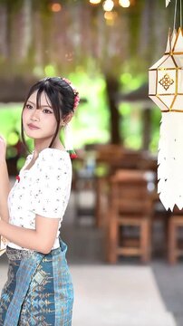 Slow motion of a beautiful Asian woman in traditional Lanna dress holding a Lanna paper lantern at Wat Ton Kwen, Chiang Mai, Thailand.