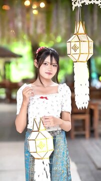 Slow motion of a beautiful Asian woman in traditional Lanna dress holding a Lanna paper lantern at Wat Ton Kwen, Chiang Mai, Thailand.