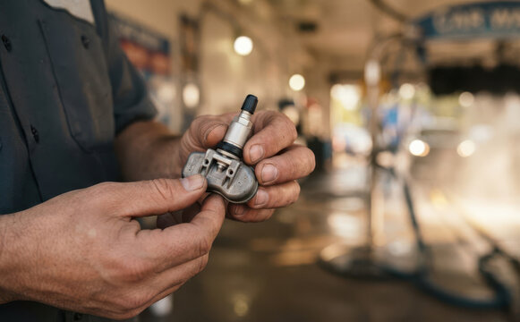 Mechanic holding a tire pressure monitoring system sensor in an auto repair shop