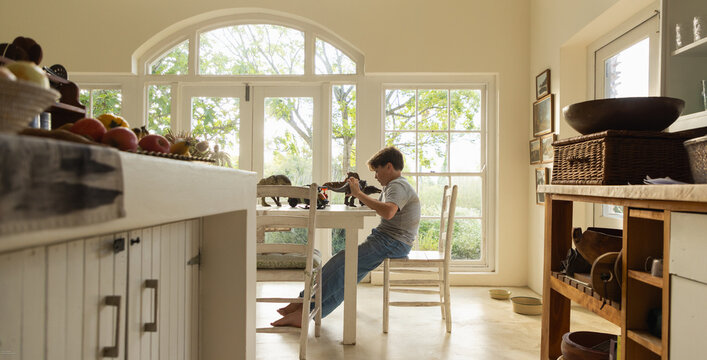 teen boy seated playing with toy dinosaurs on table in light filled room at sunset